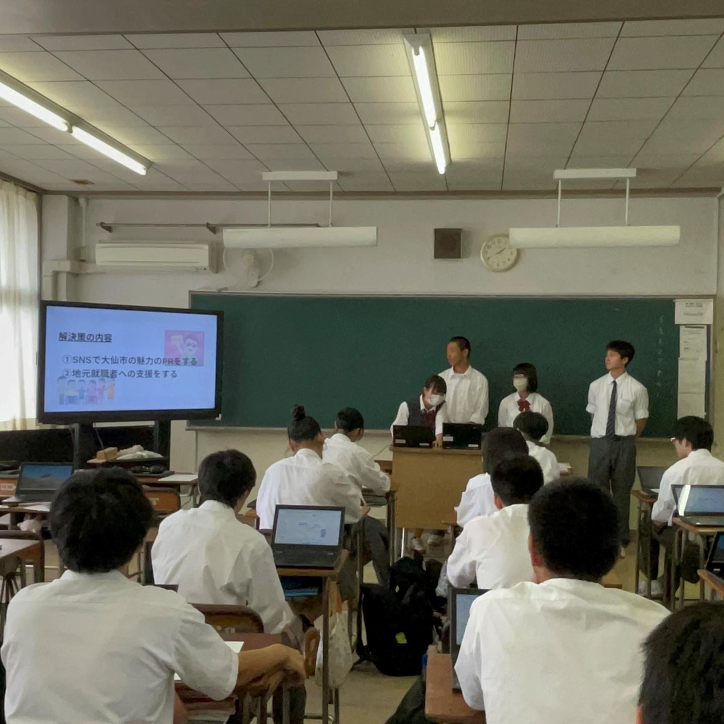 教室でモニターを使用し話し合いの結果を発表する男女4人の生徒