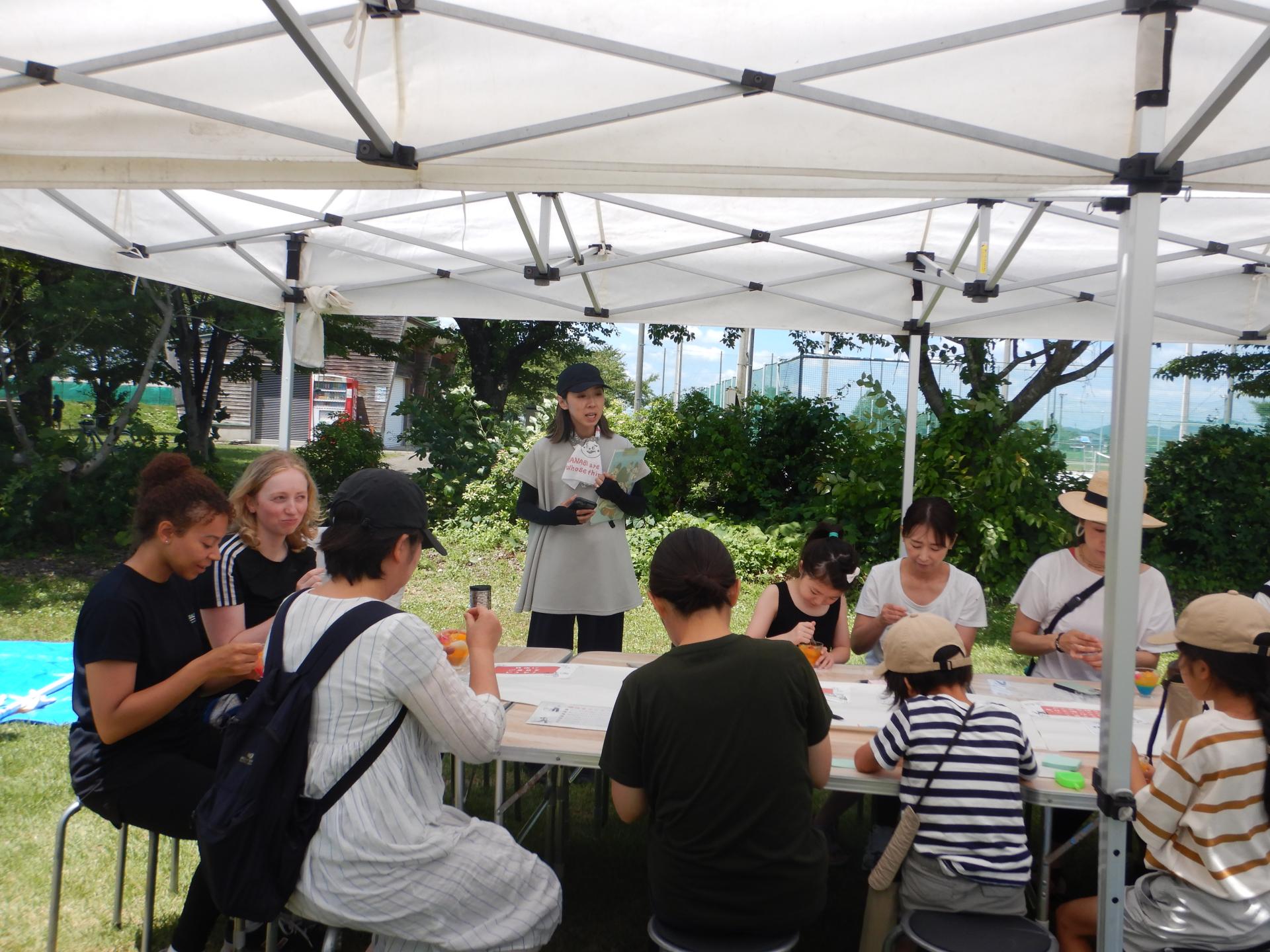 屋外のテントの下で移住者数名とトークをしながら交流する女性隊員