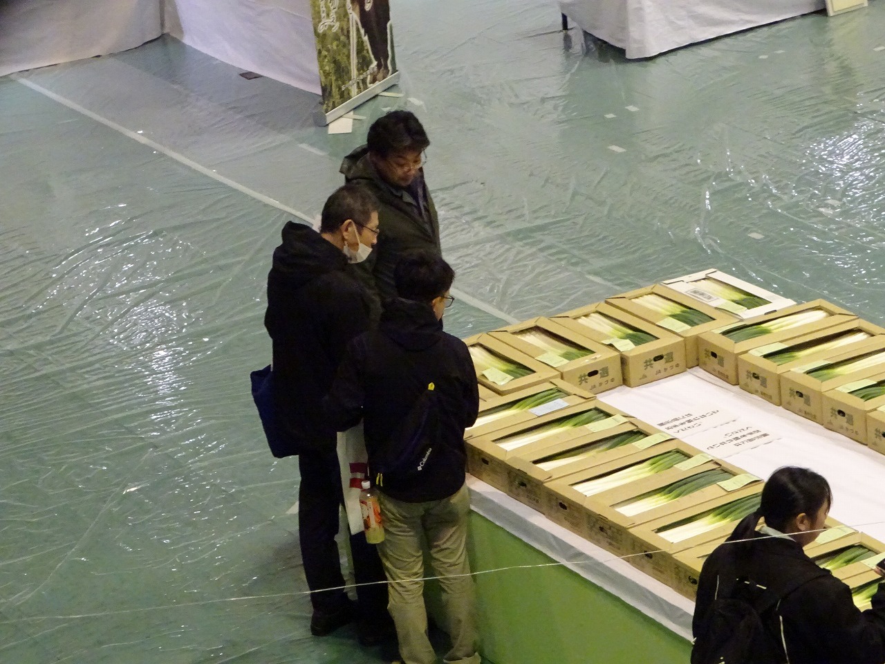 自分が出品したネギと一等のネギを見比べて先生と話をする研修生たち