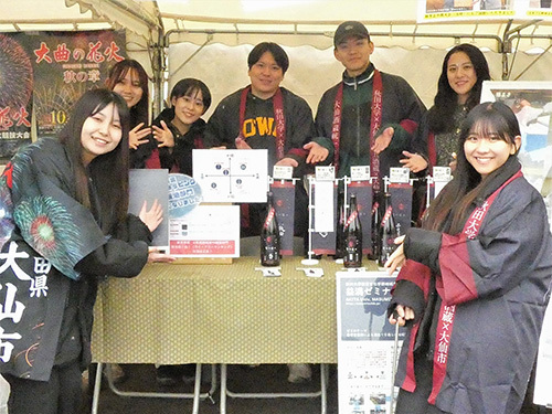 昨年の販売会の様子、男女7人の大学生がテントブース内でお酒の瓶を持って記念撮影