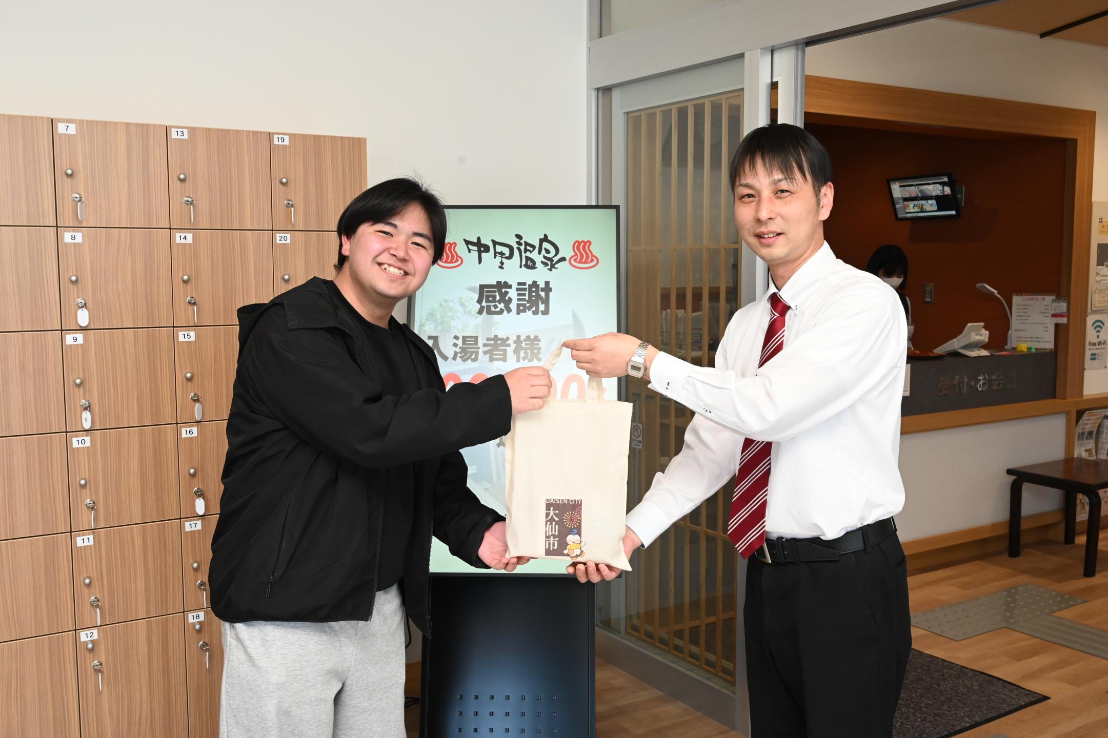 プレゼントを渡している。左に伊藤耀太さん　右に中里温泉鈴木支配人　