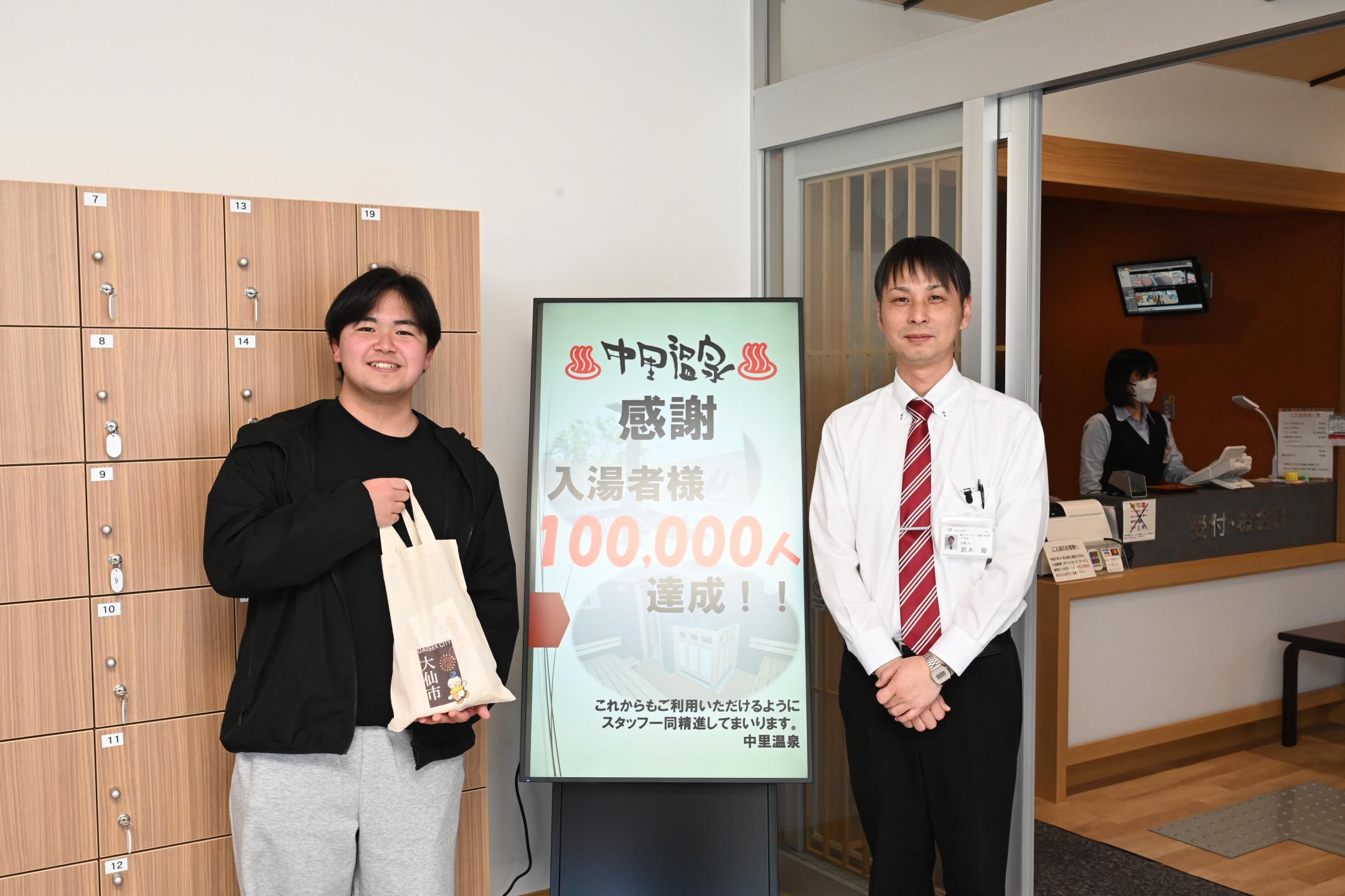 中里温泉10万人達成看板の前で写真を撮っている。