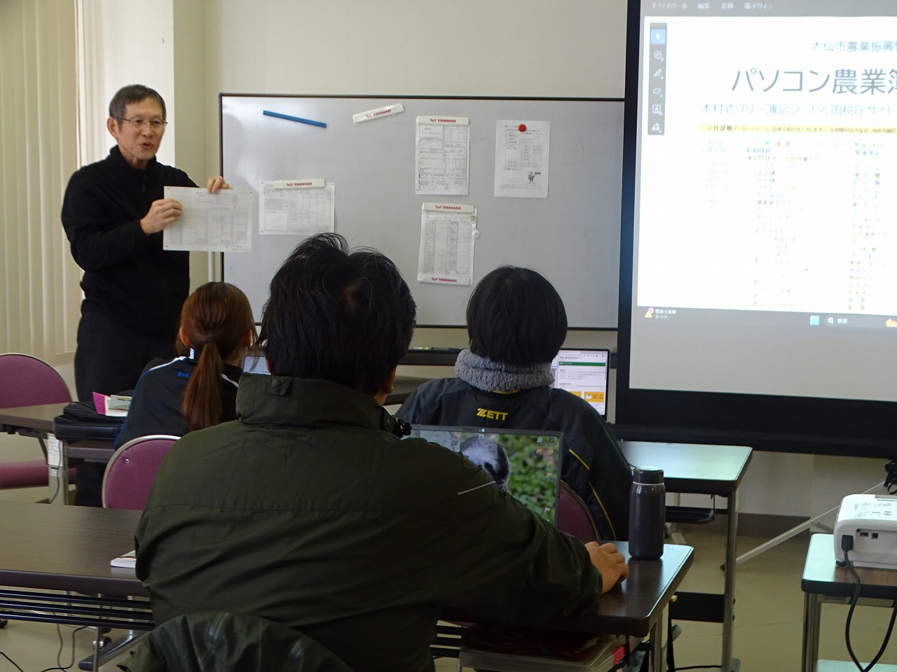 申告について学ぶ研修生、講師がスクリーンの資料を説明