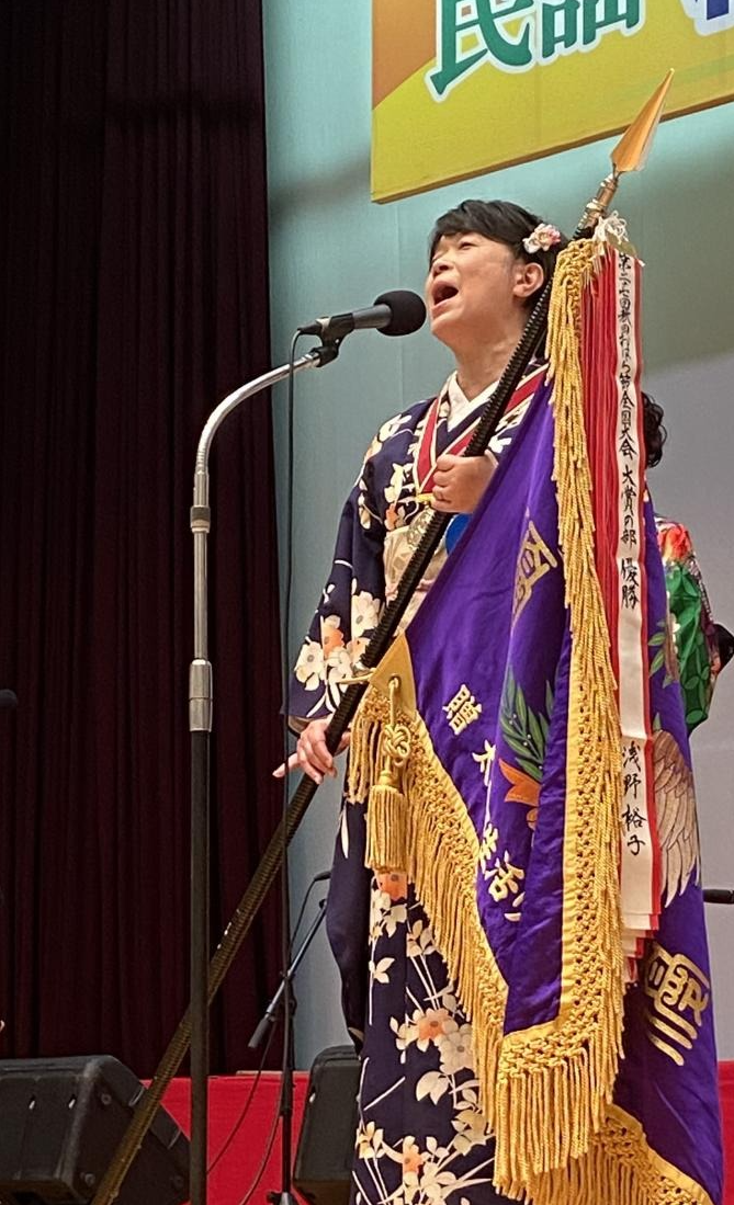 前回大会大賞の部優勝の浅野裕子さんが優勝旗を持って歌っている