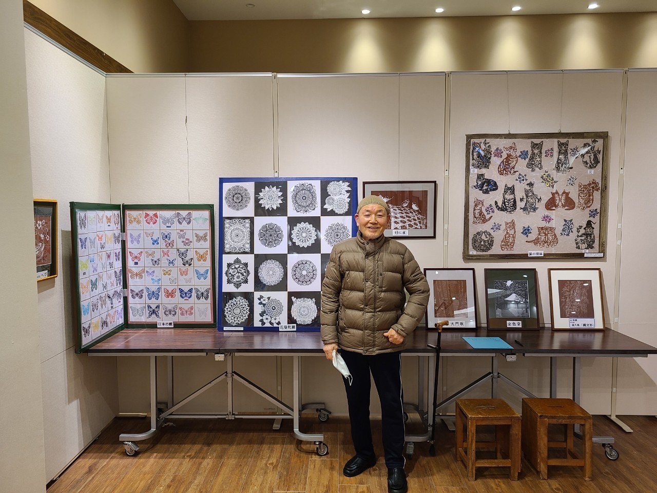 数々の切り絵作品を背景にして中央に立っている佐々木さん