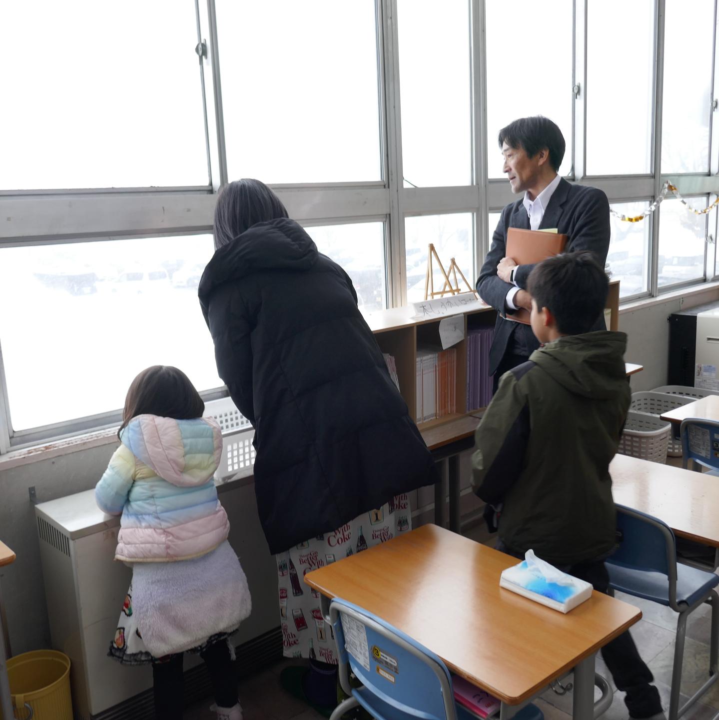 ツアー参加者のご家族、小学校の教室の窓から外の景色を眺める子ども2人とその保護者