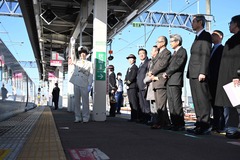 画像:JR東日本大曲駅でのおもてなしイベント、白の車掌服を着た藤井聡太竜王が手を挙げて合図している様子