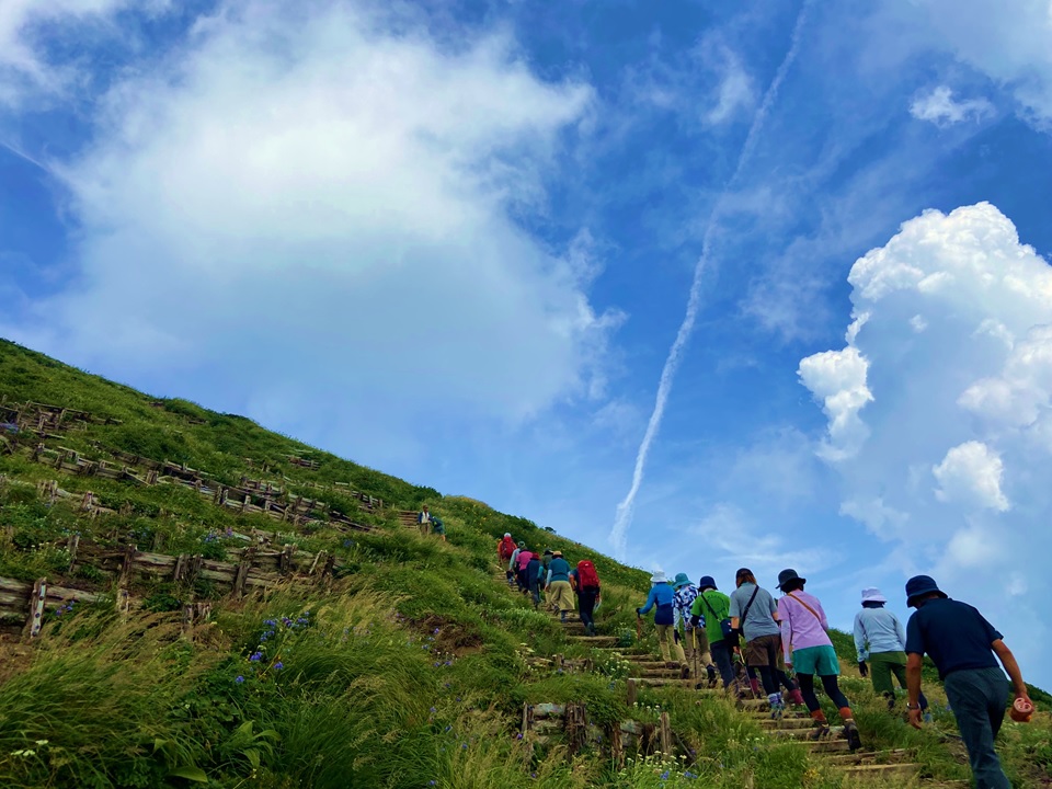 実技（登山）の様子、青空に浮かぶ白い雲を見ながら自然の雄大さを感じる受講生