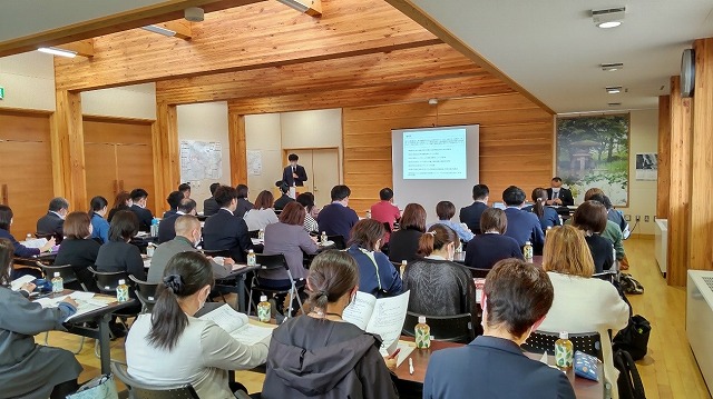 人々が椅子に座り、資料を手に話を聞いている様子