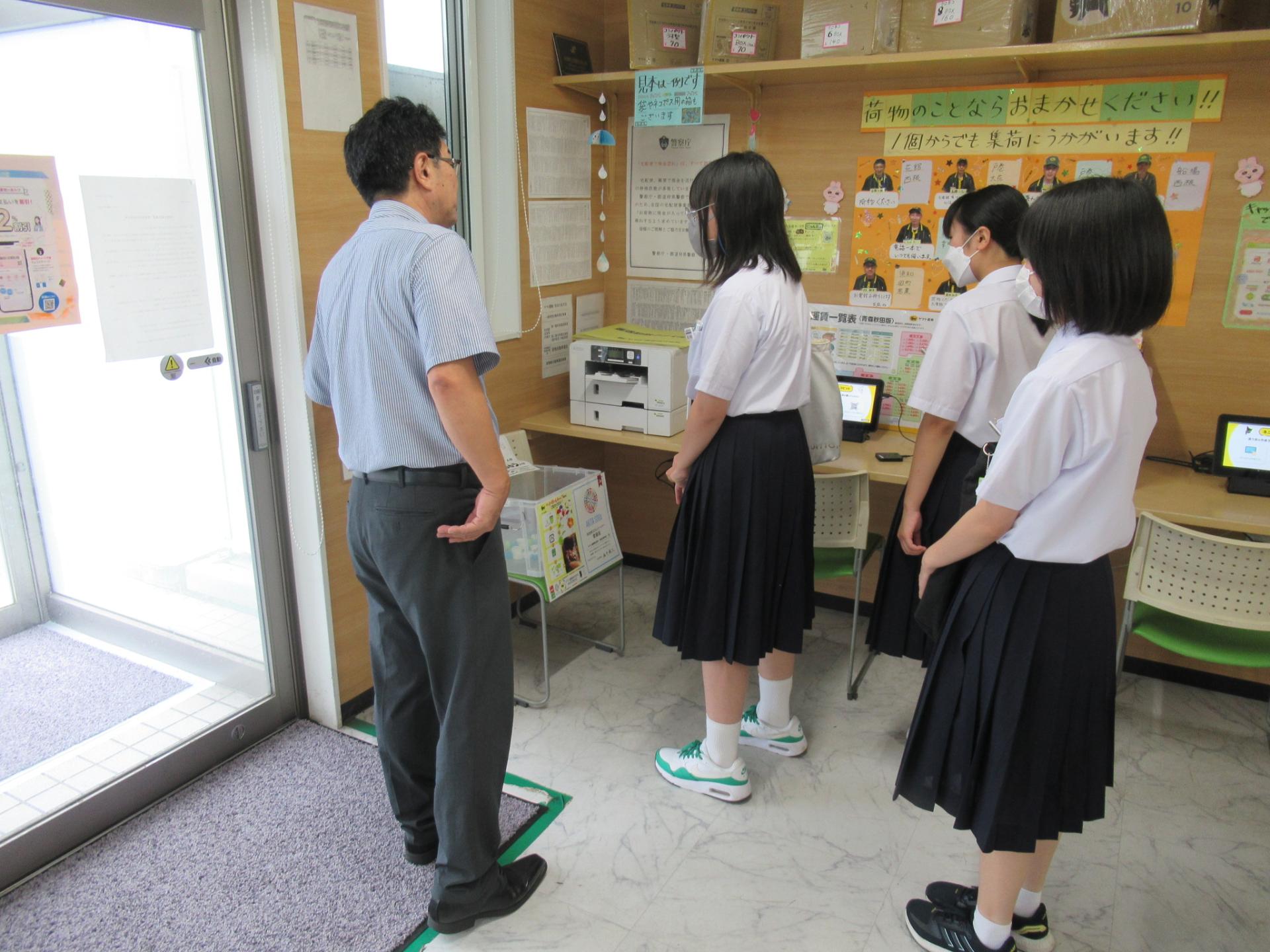 ヤマト運輸での勉強会の様子（実際の商品を手に取り担当者の説明を聞くレポーター3人）