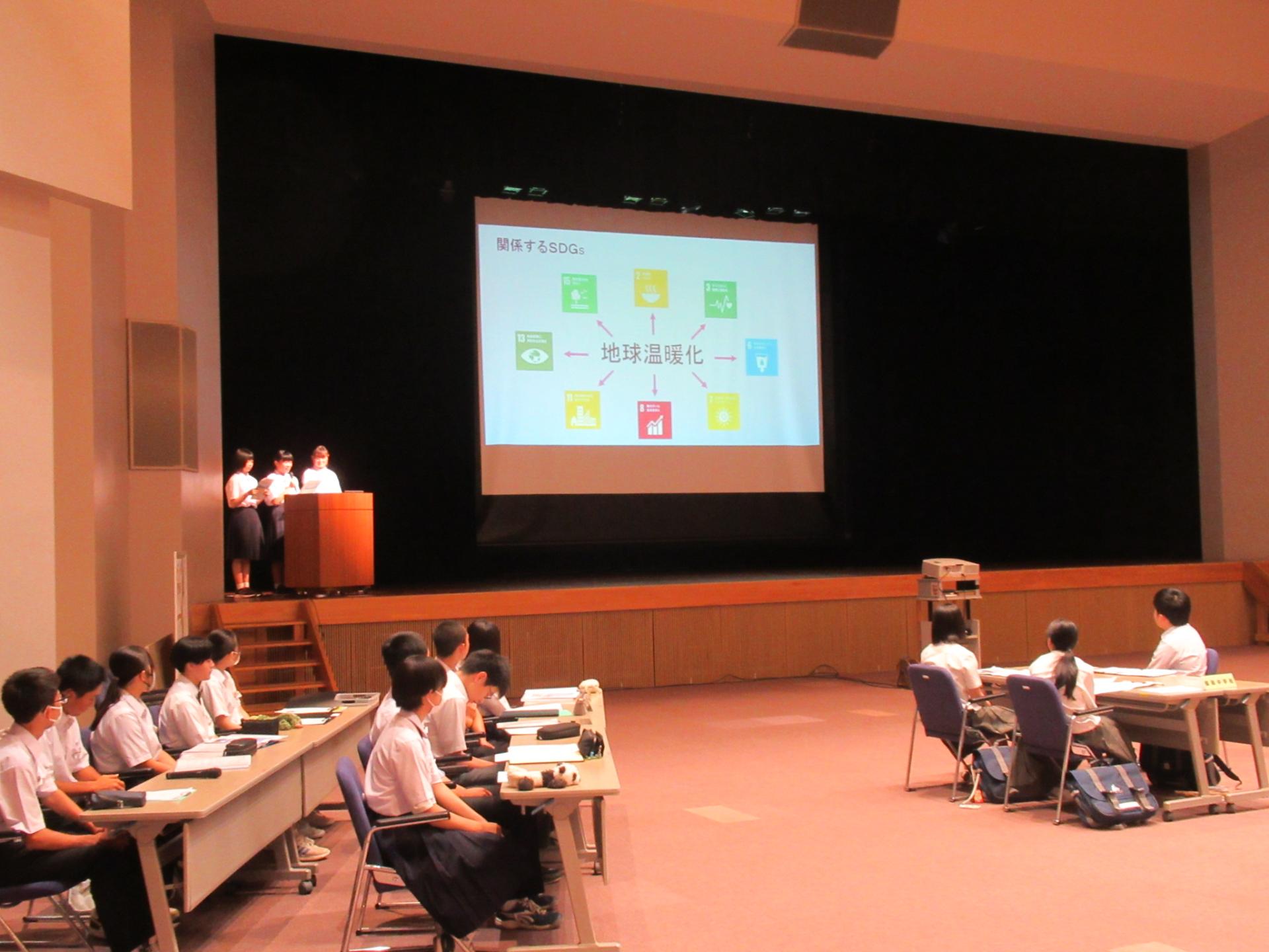 中学生サミット（ステージに設置されたスクリーンに投影した資料をもとに説明する中学生）