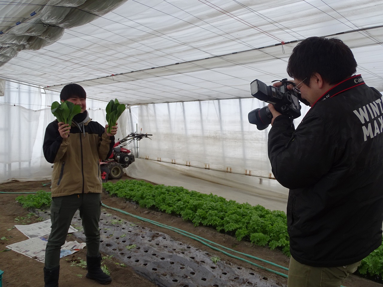JA広報担当者が野菜をかかげポーズをとる研修生を撮影している様子