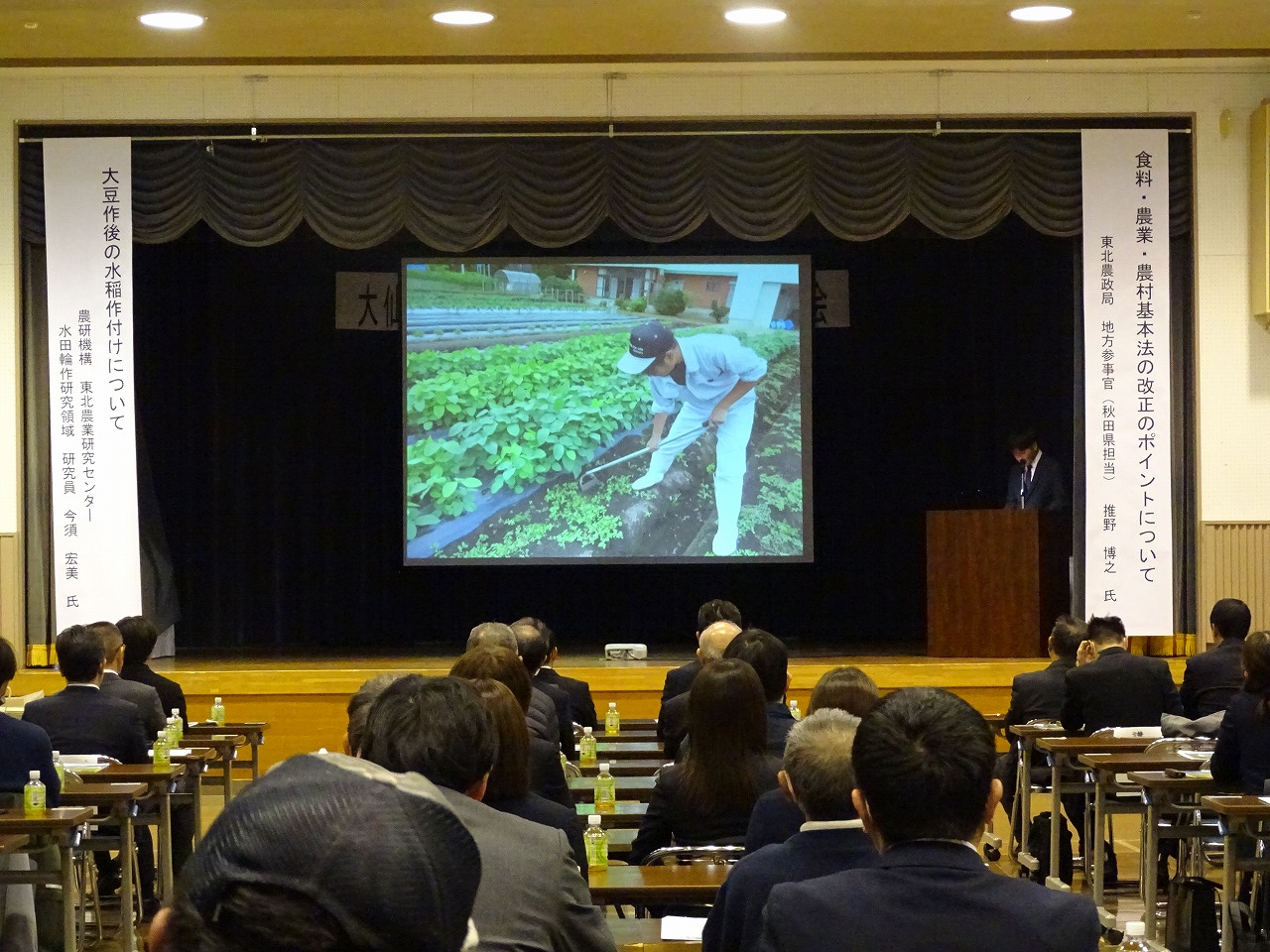 ステージ上でスライドを活用し研修発表をしている男性研修生