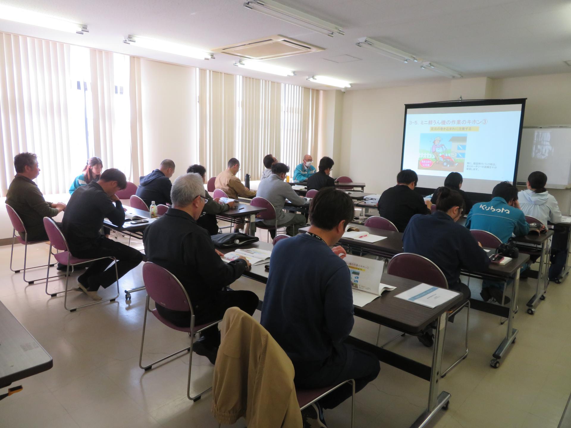 座学の様子、スクリーンの資料を見ながら説明を受けている