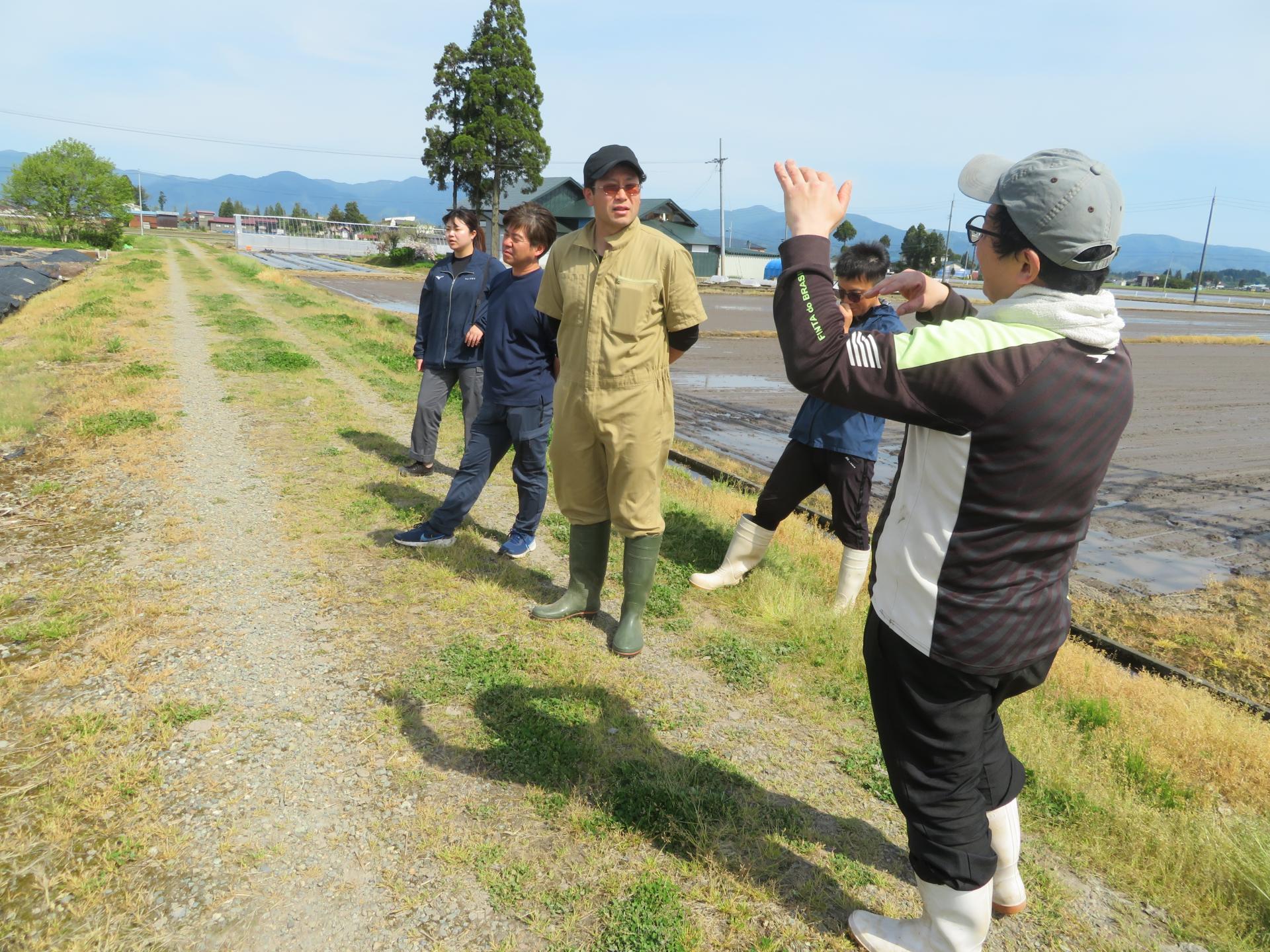 アスパラガスを露地栽培している研修修了生の先輩から、管理方法について説明を受ける研修生たち