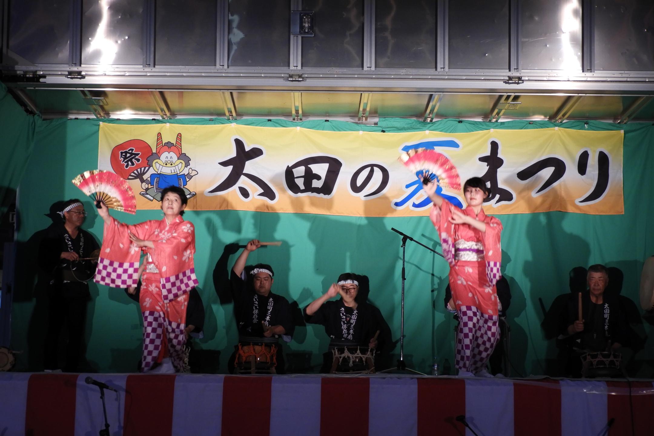 舞台上で着物を着て扇子を持って踊る女性2人