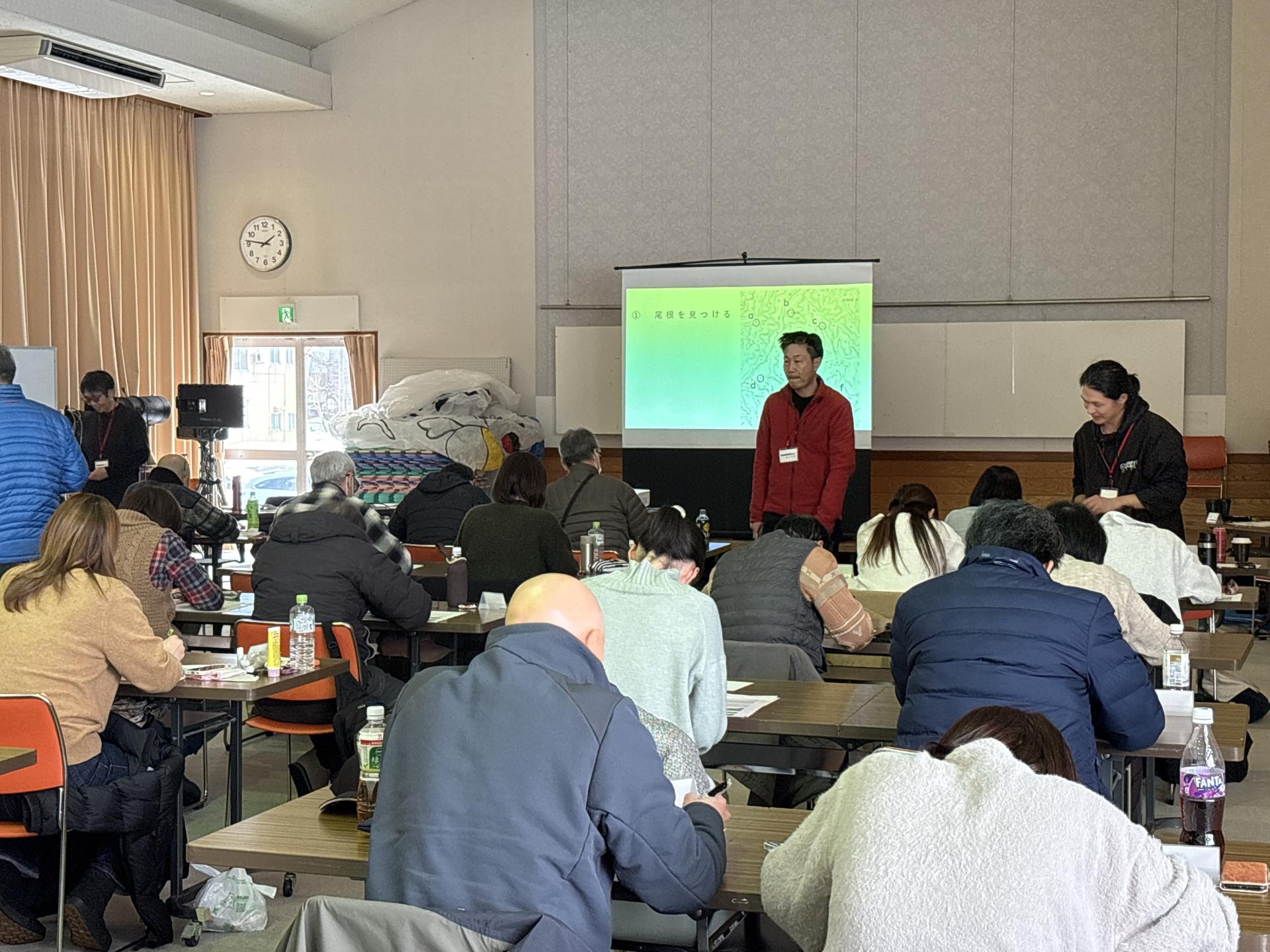 昨年の座学の様子、スライドを使って説明する講師、それを真剣に聞く受講生