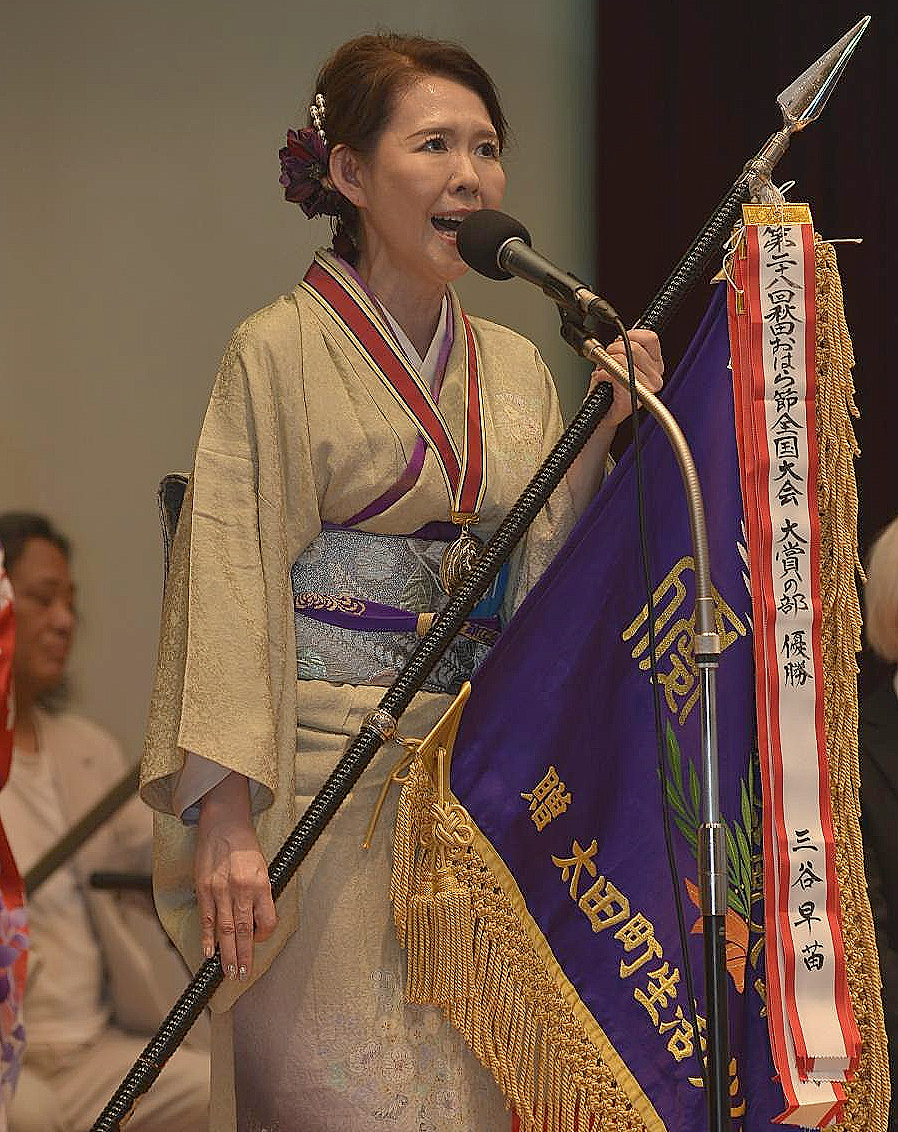 大賞の部優勝の三谷さん、優勝旗を持って歌唱している